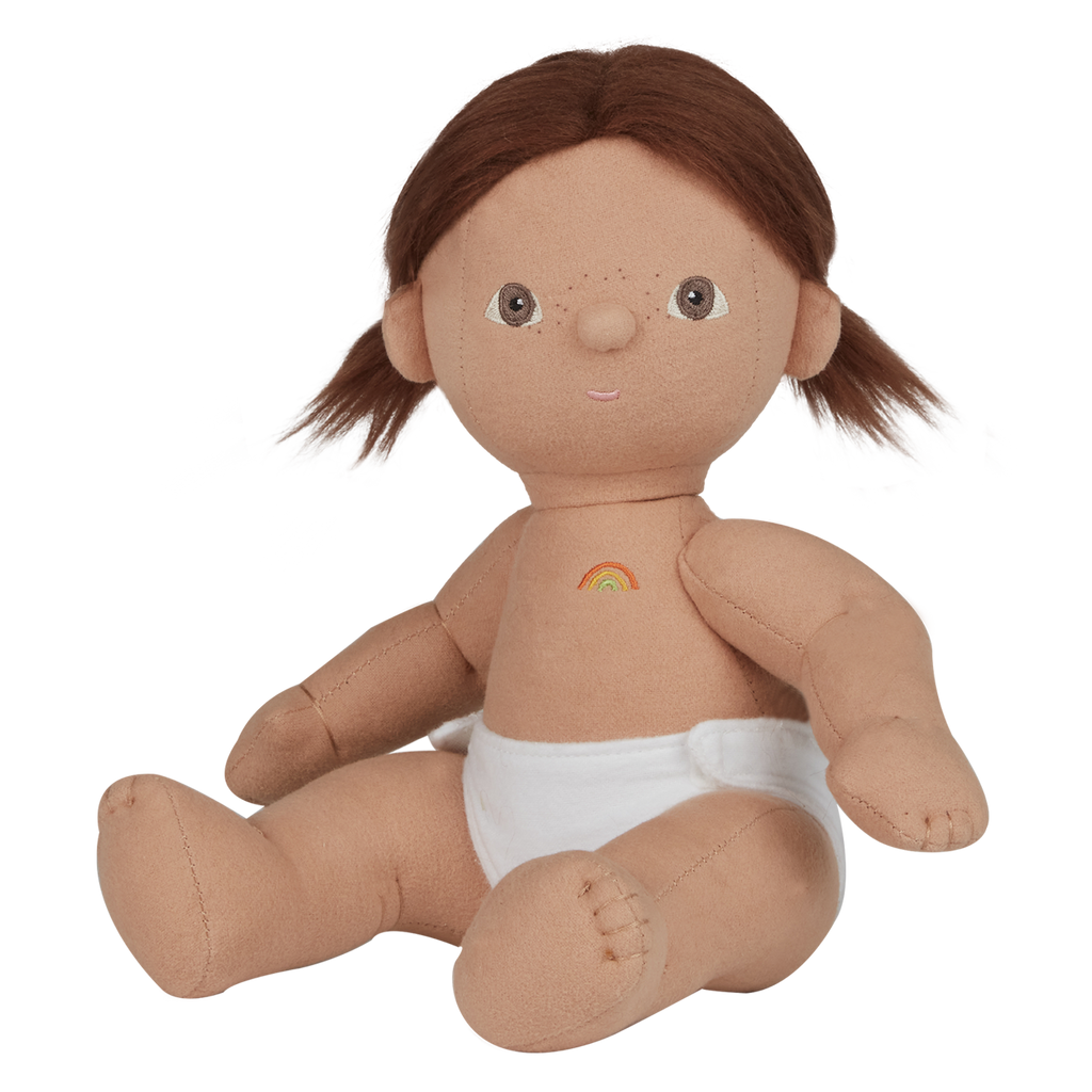 A soft, fabric doll with brown pigtails stands against a white background. It wears a pink romper and brown shoes, conveying a playful and charming tone.