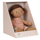 A soft, fabric doll with brown pigtails stands against a white background. It wears a pink romper and brown shoes, conveying a playful and charming tone.