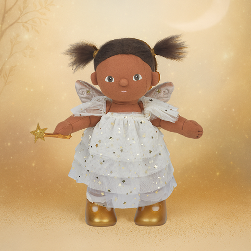 Brown-skinned fairy doll with pigtails, wearing a white starry dress and gold boots, holds a star wand. Background features a warm, golden glow.