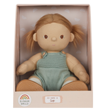 A soft doll with brown hair in pigtails sits in a pastel box. The doll wears a knitted green romper and is labeled "Gigi" with a cheerful expression.
