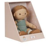 A soft doll with brown hair in pigtails sits in a pastel box. The doll wears a knitted green romper and is labeled "Gigi" with a cheerful expression.