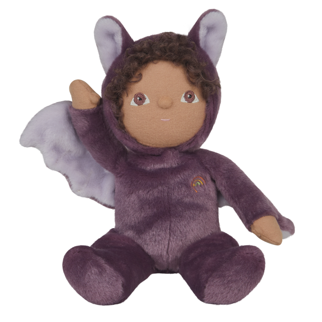 Plush toy dressed as a purple bat with fluffy wings, curly hair, and a friendly smile. A small rainbow emblem is on the chest. White background.