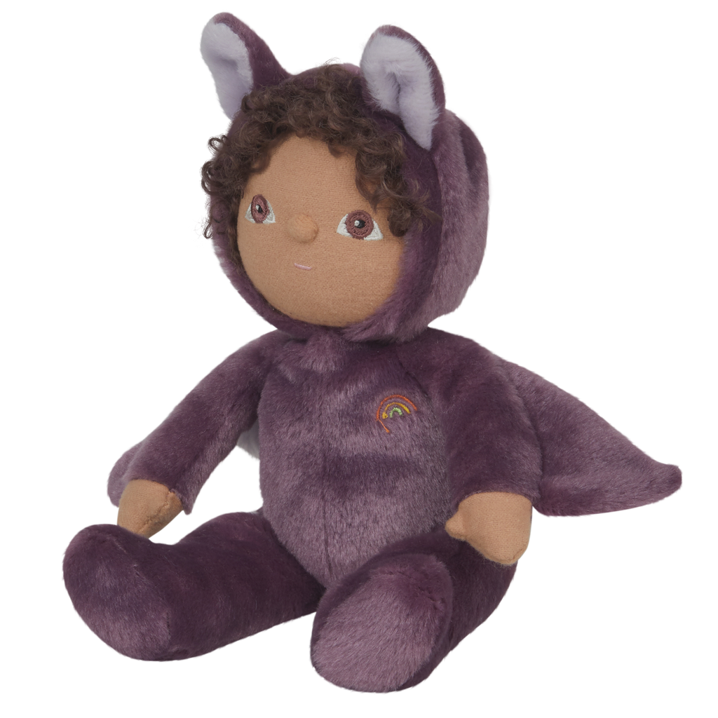 Plush toy dressed as a purple bat with fluffy wings, curly hair, and a friendly smile. A small rainbow emblem is on the chest. Black background.