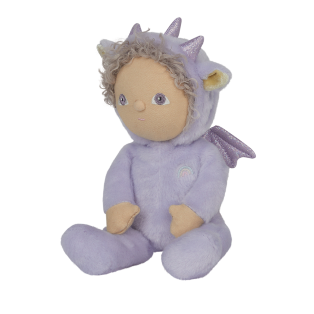 A plush doll wearing a lavender dragon costume with sparkly ears and horns. The doll has curly hair, a serene expression, and a rainbow emblem.