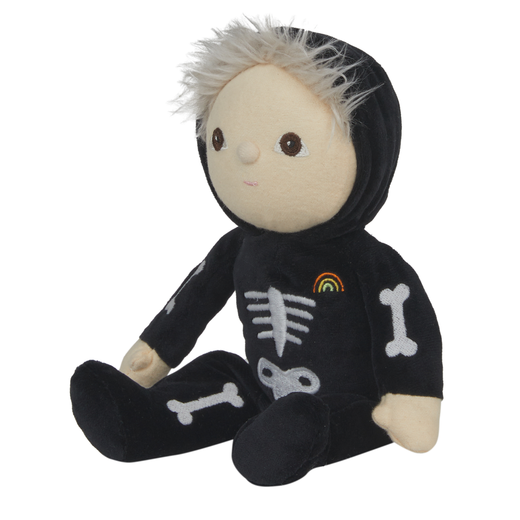 Cute plush doll with light hair in a black skeleton costume, featuring bone designs and a small rainbow patch. The doll has a neutral expression.