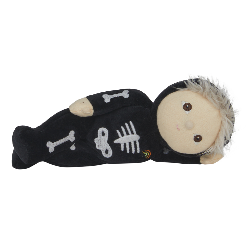Cute plush doll with light hair in a black skeleton costume, featuring bone designs and a small rainbow patch. The doll has a neutral expression.