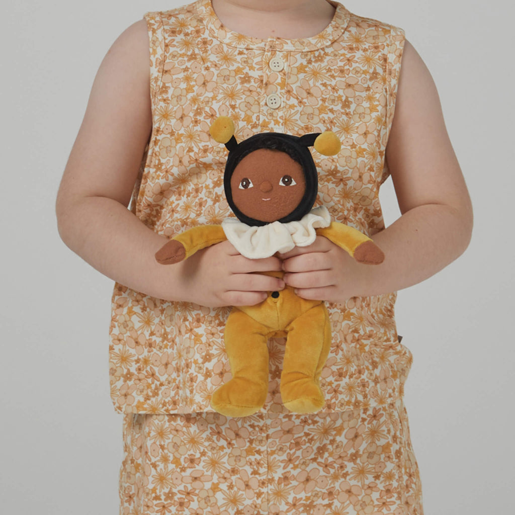 Plush doll dressed as a bee, featuring a black head with bee antennae, a white ruffled collar, and yellow outfit with wing details.