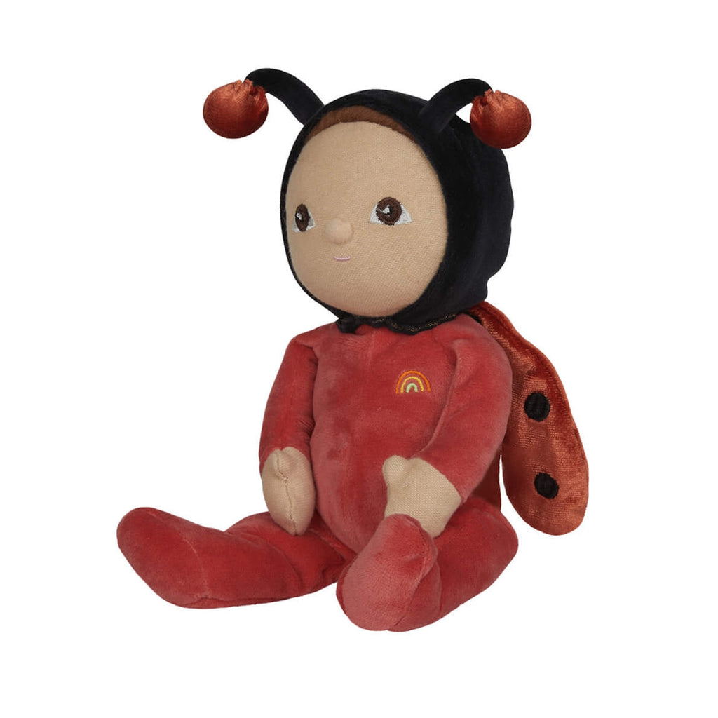Soft plush toy resembling a ladybug figure, wearing a red outfit with a rainbow patch. Features a gentle facial expression and antennae on its hood.