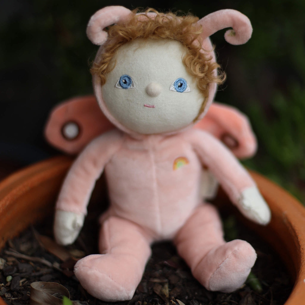 Soft plush doll with curly hair and blue eyes, dressed in a pink butterfly costume with wings and antennae. A small rainbow is embroidered on the outfit.