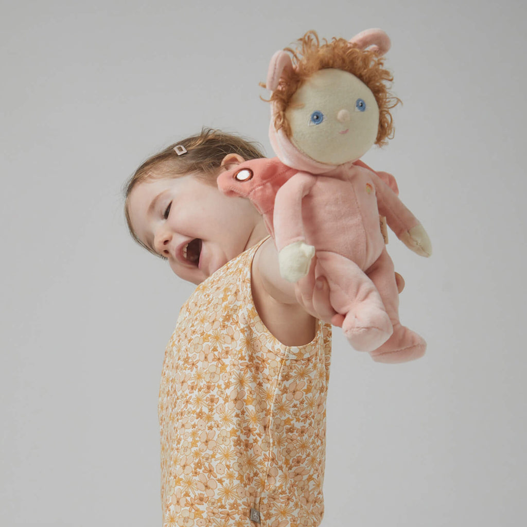 Soft plush doll with curly hair and blue eyes, dressed in a pink butterfly costume with wings and antennae. A small rainbow is embroidered on the outfit.