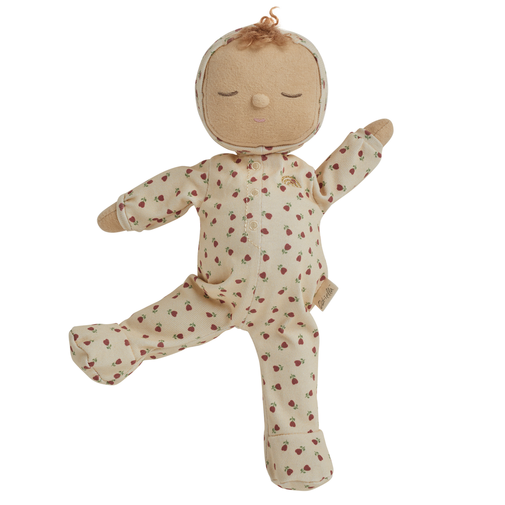 A soft doll in a cream-colored outfit with red strawberry patterns. The doll has closed eyes, curly hair on top, and small mittens and booties.