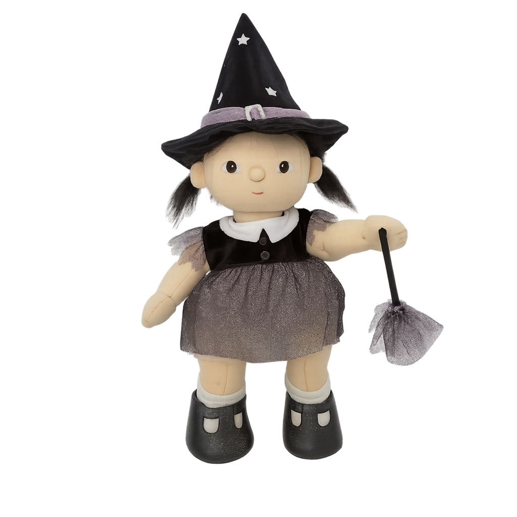 A plush doll dressed as a witch features a pointy black hat with stars, a gray dress, and black shoes. The doll holds a small broom, creating a playful, whimsical tone.