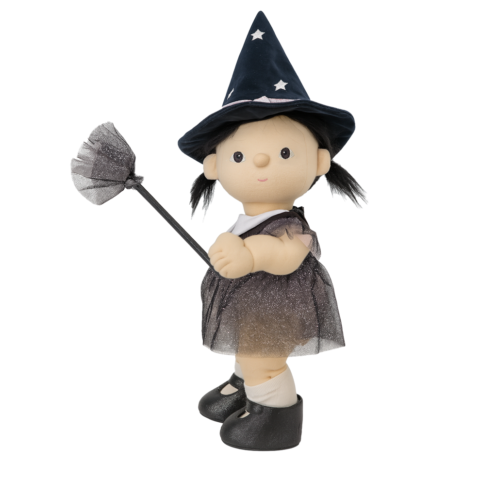 A plush doll dressed as a witch features a pointy black hat with stars, a gray dress, and black shoes. The doll holds a small broom, creating a playful, whimsical tone.