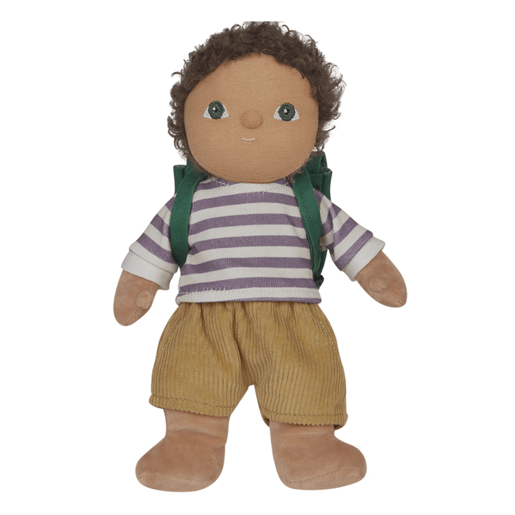 A plush doll with curly hair, wearing a purple striped shirt, tan corduroy pants, and a green backpack, stands against a white background.