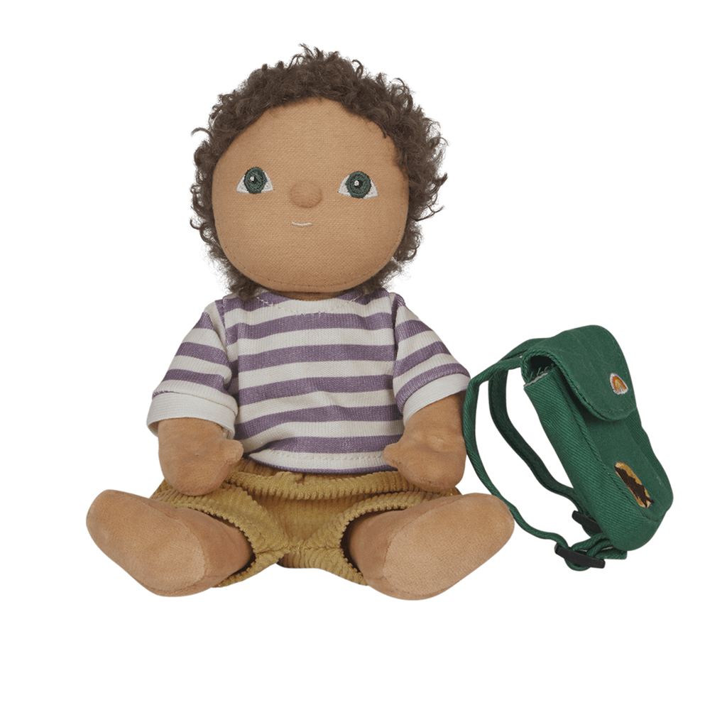 A plush doll with curly hair and wide eyes wears a striped purple and white shirt and brown shorts. It sits beside a small green backpack, all set against a white background. The scene is playful and inviting.