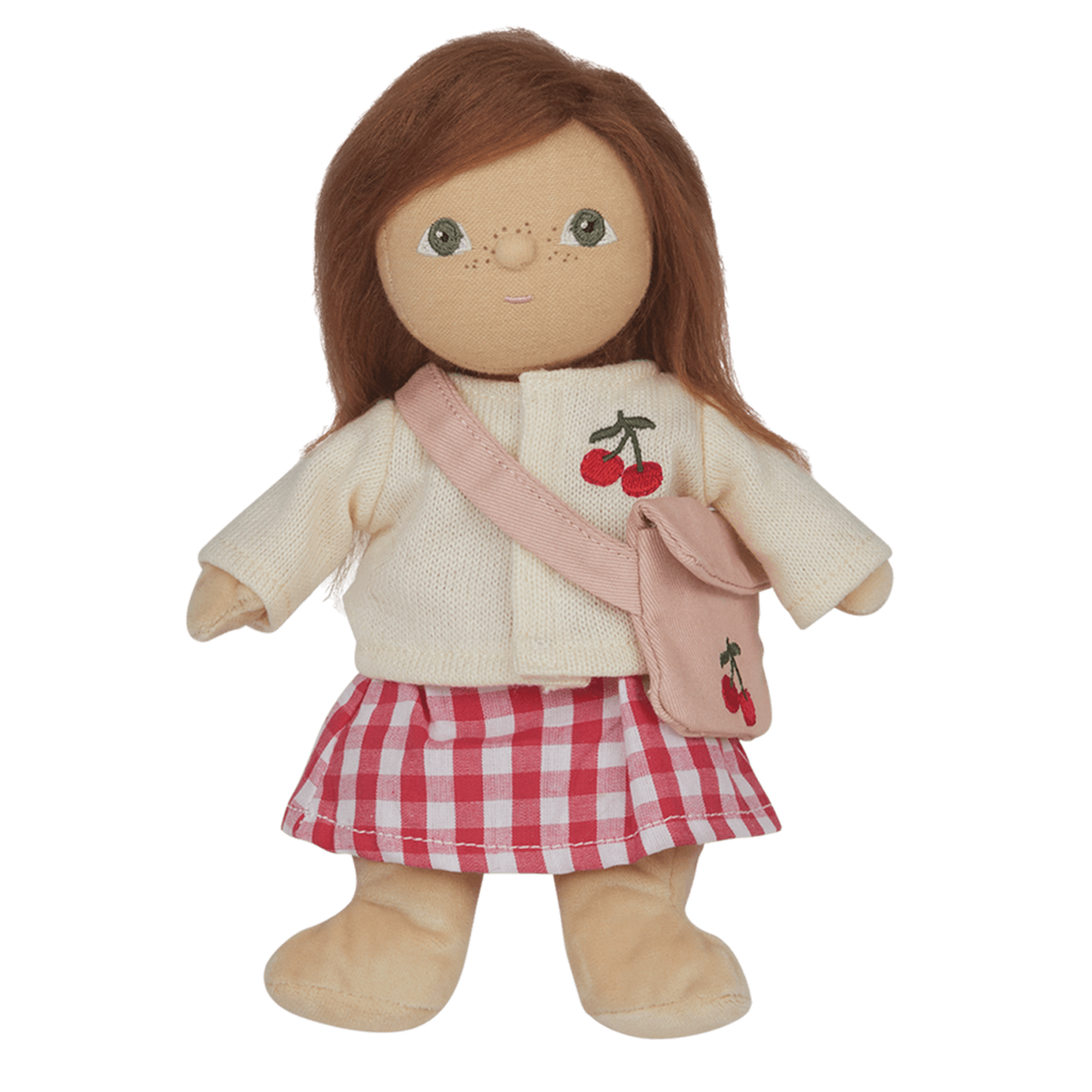 A soft, brown-haired doll wearing a cream sweater with a cherry design, pink checked skirt, and matching cherry bag, set against a white background.