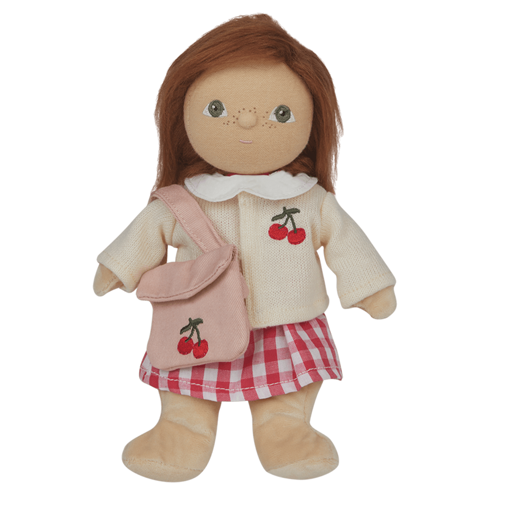 A soft, brown-haired doll wearing a cream sweater with a cherry design, pink checked skirt, and matching cherry bag, set against a white background.