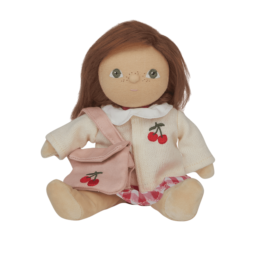 A soft, brown-haired doll wearing a cream sweater with a cherry design, pink checked skirt, and matching cherry bag, set against a white background.