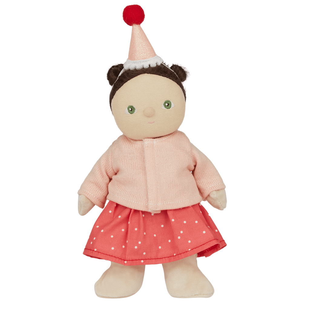 A cute doll wearing a pink sweater, red polka dot skirt, and party hat with a pom-pom smiles against a white background. Whimsical and festive.