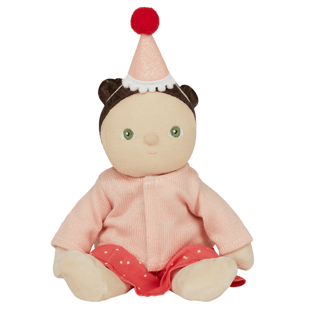 A cute doll wearing a pink sweater, red polka dot skirt, and party hat with a pom-pom smiles against a white background. Whimsical and festive.