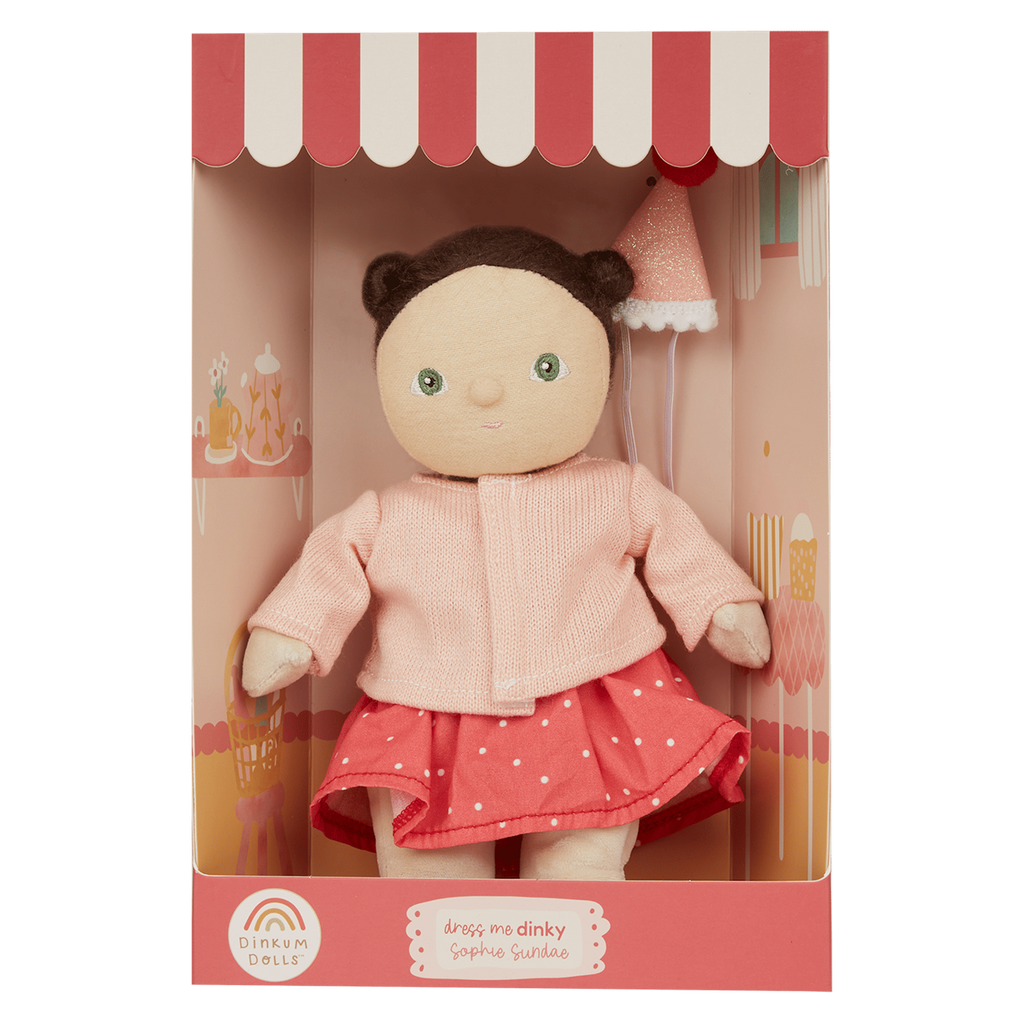 A cute fabric doll with brown hair buns, dressed in a pink top and polka dot skirt, is displayed in a striped gift box with whimsical designs.
