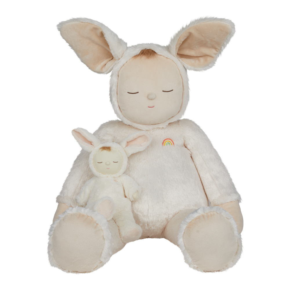 A plush toy with closed eyes, wearing a soft, white bunny suit with large ears. It has a small rainbow patch on its chest, conveying calmness.