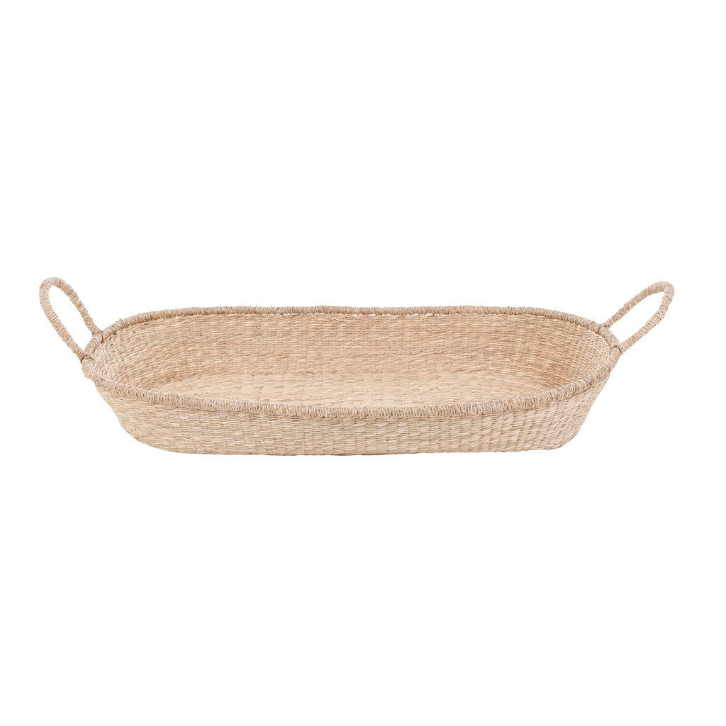 A natural baby changing basket with two loop handles on each side. The basket is oval-shaped, with a simple, rustic texture and a neutral, earthy tone.