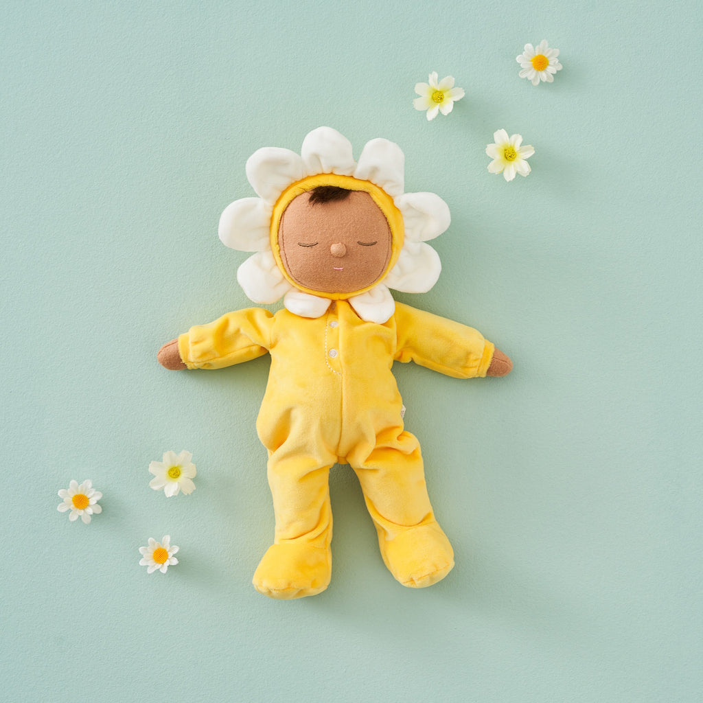 A plush doll with a light brown face framed by white petals, resembling a flower. It wears a soft, yellow bodysuit, conveying a calm, playful vibe.