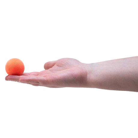 A small, fuzzy orange Teenie NeeDoh ball resting on the fingertips of an open, outstretched hand.