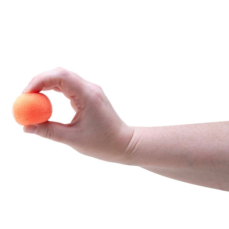 A hand holding a small, textured orange Teenie NeeDoh Fuzz Ball between two fingers against a white background.