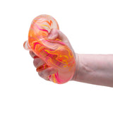 Hand squeezing a NeeDoh Niceberg Swirl stress ball with orange, pink, and yellow marble patterns on a white background.