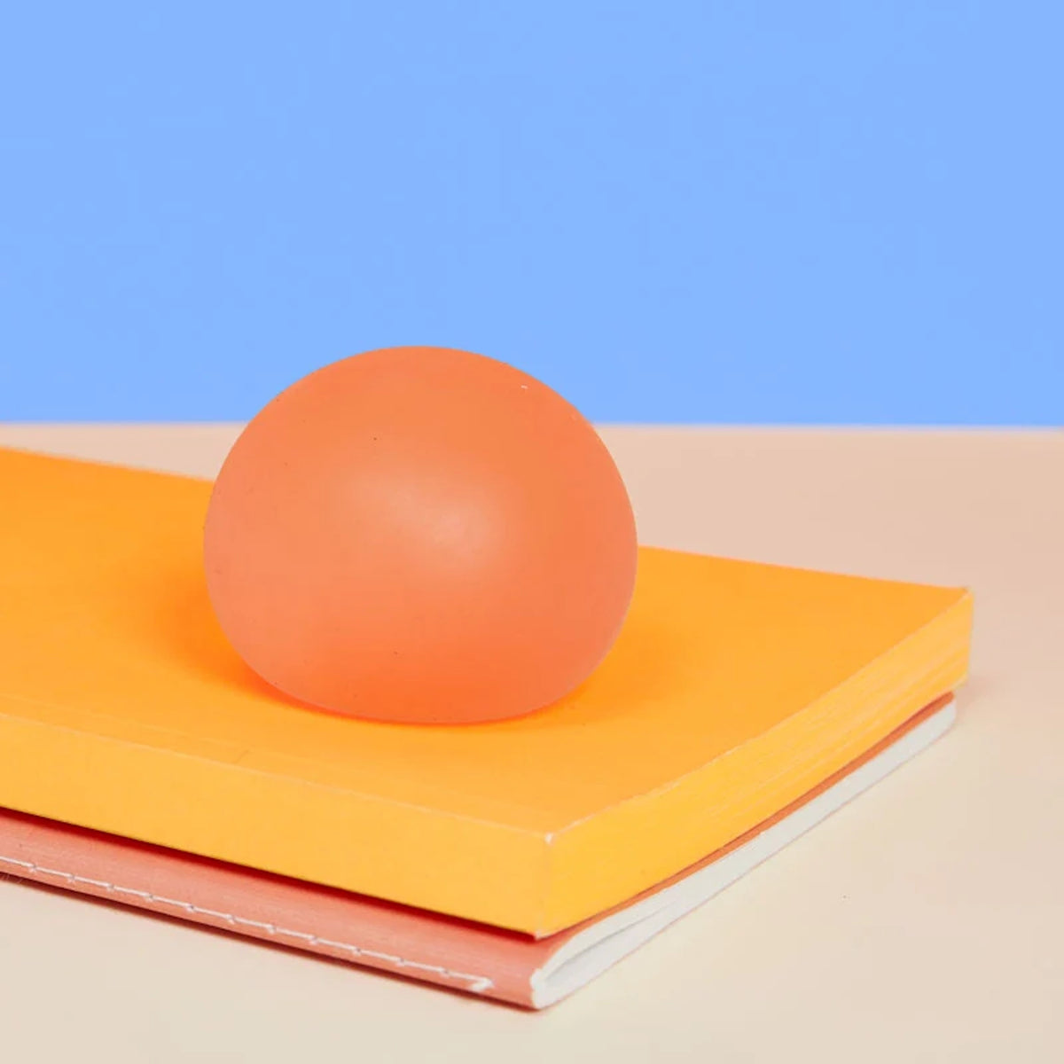Round orange stress toy resting on a stack of colorful notebooks against a blue background.