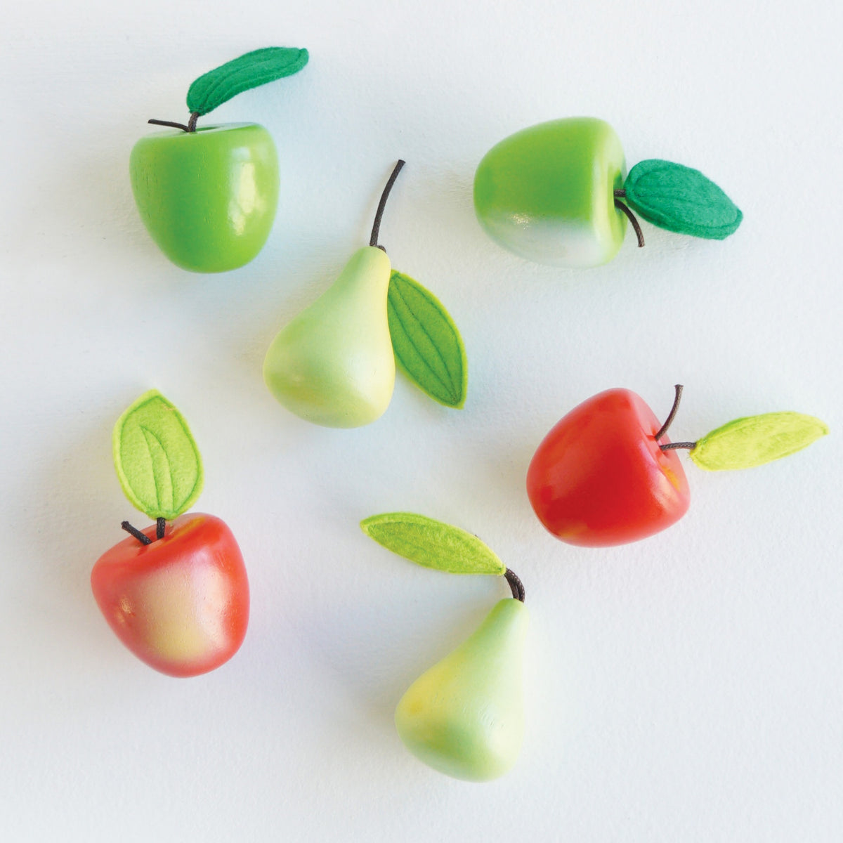 Toy wooden apples and pears with felt leaves arranged on a white background.