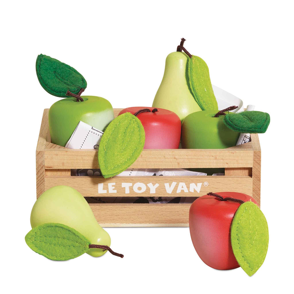 Wooden crate labeled "Le Toy Van" filled with brightly colored toy apples and pears, some red, some green. Felt leaves add a playful touch.