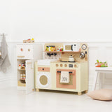 Wooden toy play kitchen setup with an open fridge, microwave, oven, and accessories in a bright room.