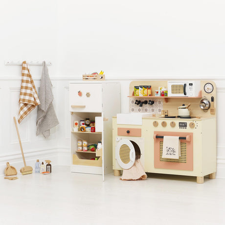 Wooden toy play kitchen setup with open fridge, play broom set, and accessories in a bright room.