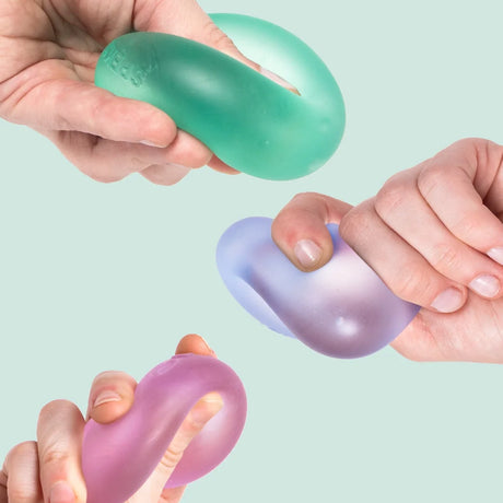 Three hands squeezing squishy, cool-toned memory gel stress balls against a light mint background.