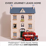 Wooden dollhouse and red double-decker bus with Paddington figure. Text: "Every journey leads home".