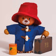 Wooden Paddington Bear figure wearing a red hat and blue coat, holding a brown suitcase labeled "P.B."