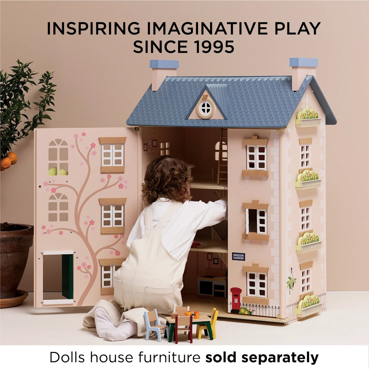 Child playing with an open wooden dollhouse featuring a blue roof and furniture outside.