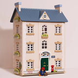 Three-story wooden dollhouse with a blue roof, green door, and Paddington Bear standing out front.