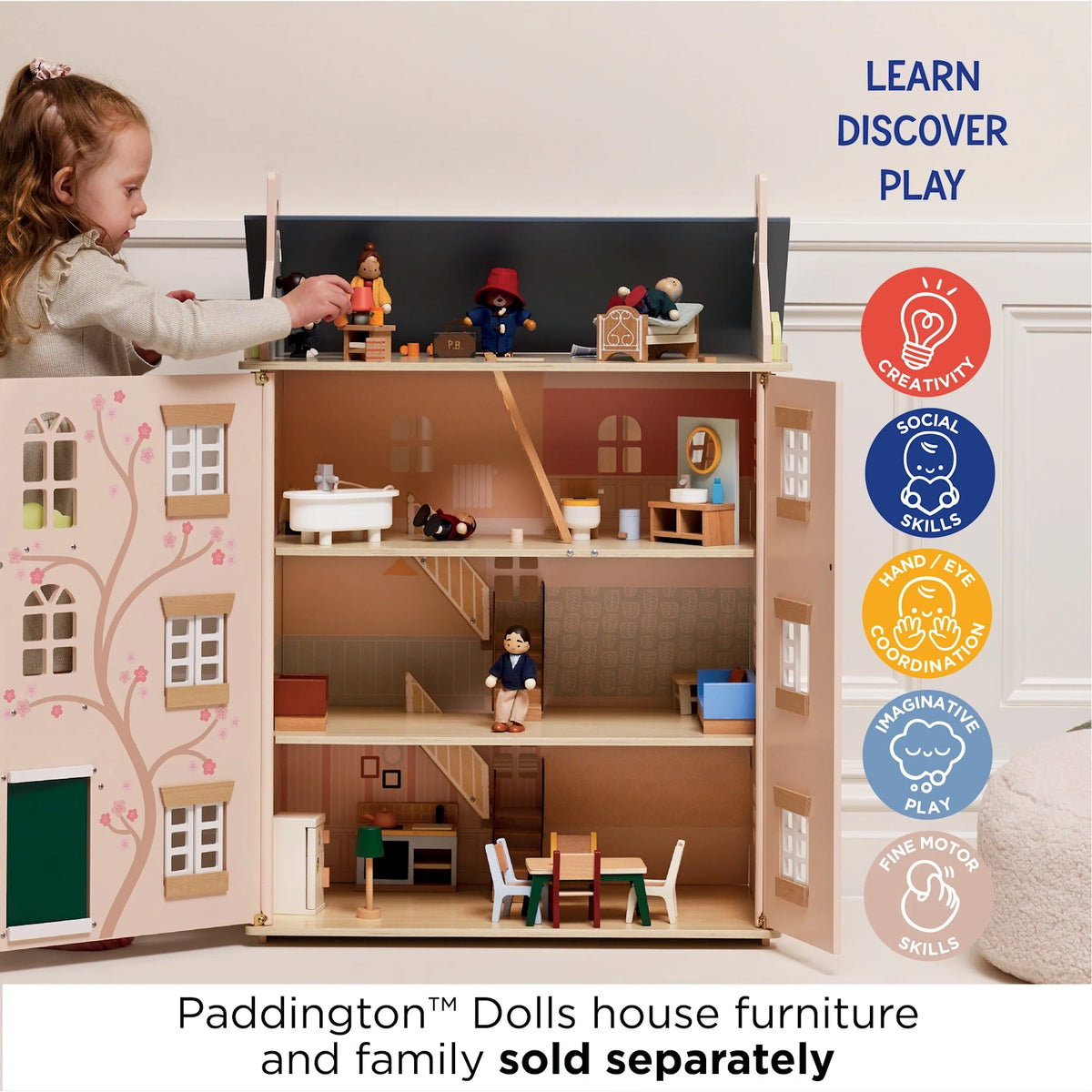 Young girl playing with a wooden dollhouse filled with miniature furniture and figures.