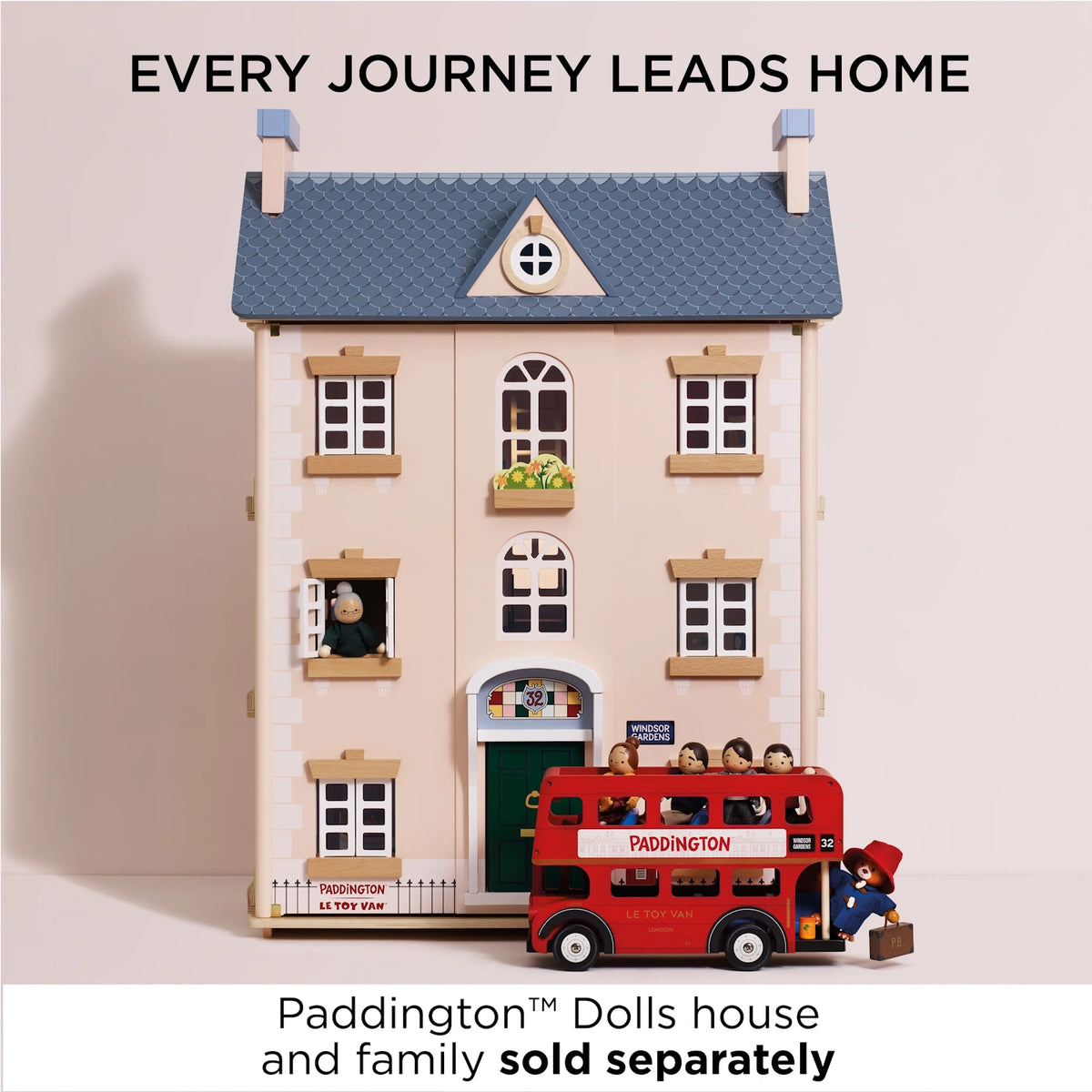 A pink wooden toy dolls house with a blue roof, alongside a red London double-decker bus toy with a Paddington family.