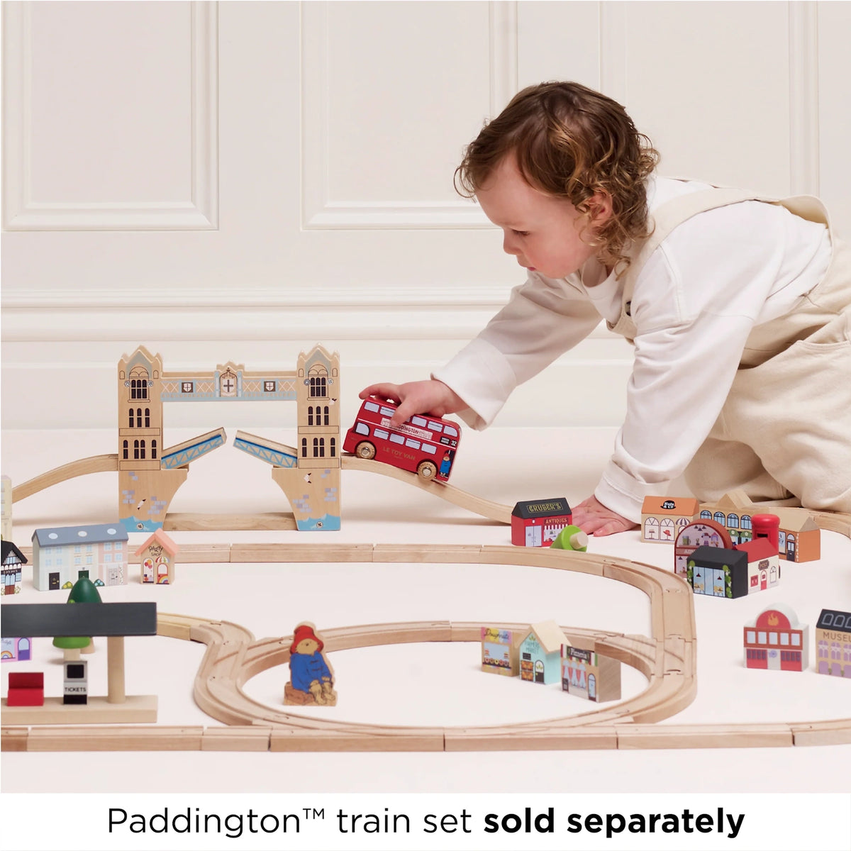 A toddler playing with the Paddington toy bus on a wooden train and bridge track set.