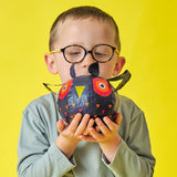 Child with glasses holds a colorful owl balloon against a bright yellow background, conveying curiosity and playfulness.