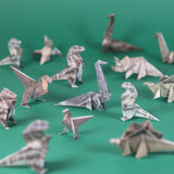 A variety of patterned origami paper dinosaurs arranged across a plain green surface.