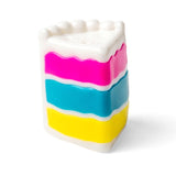 Plastic toy slice of cake with pink, blue, and yellow layers and white frosting, on a white background.