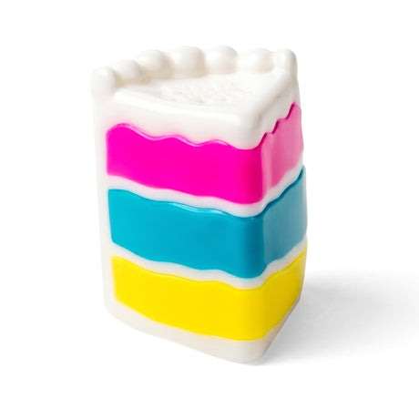 Plastic toy slice of cake with pink, blue, and yellow layers and white frosting, on a white background.