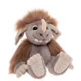 Plush monster toy with grey fur, brown mane, single horn, big floppy ears, and prominent teeth, sitting down.