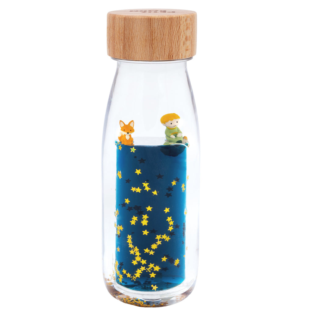 A glass bottle with a wooden lid contains blue liquid and floating golden stars. Miniature figures of a child and a fox sit atop, conveying whimsy.